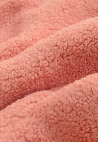 Měkká růžová fleecová látka s hustou, kudrnatou a nadýchanou texturou tvořící jemné záhyby.