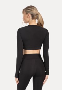 Top corto nero a maniche lunghe con design aderente e collo alto, realizzato in tessuto liscio, abbinato a leggings a vita alta coordinati.