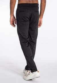 Pantalones negros de corte estrecho con un acabado de tela suave. Presentan dos bolsillos traseros y un diseño limpio en la cintura. Estilizados con zapatillas blancas.