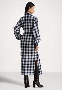 Garas piedurknes pleda kleita tumši zilā un baltā krāsā ar jostu viduklī, sānu šķēlumu un bumbuļpiedurknēm. Izgatavota no mīksta auduma ar klasisku rūtiņu rakstu.