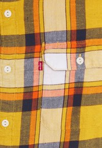 Camicia a quadri gialla in cotone, con check arancioni, neri e bianchi, tasca frontale e bottoni bianchi. Inclusa etichetta rossa Levi's.