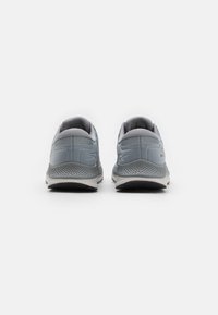 Baskets de sport grises avec une tige en mesh, un col rembourré et une semelle texturée. Présente un logo subtil à l'arrière et des accents clairs contrastés.