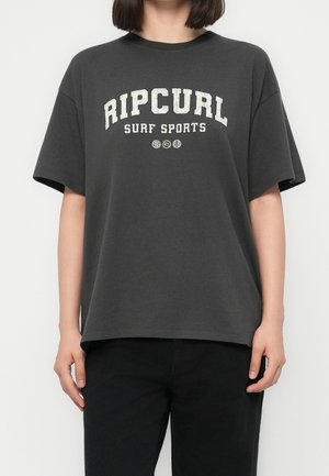 Person wearing a loose dark gray T-shirt with "RIP CURL SURF SPORTS" text and three small circular icons below the text.