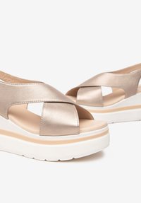 Sandali platform metallici oro con design a fascetta incrociata, parte superiore testurizzata e suola bianca. Presentano una soletta imbottita e punta aperta.