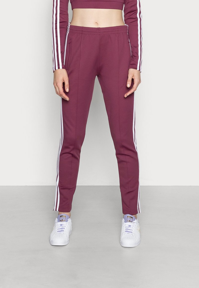 Pantaloni sportivi bordeaux con strisce bianche sui lati, vita elastica e vestibilità slim. Abbinati a sneaker bianche. Tessuto liscio.