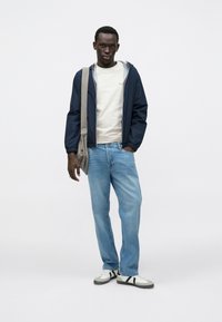 Ναυτικό αδιάβροχο με ελαστικές μανσέτες, ανοιχτό γκρι φούτερ με κουκούλα, ανοιχτό μπλε τζιν, γκρι και λευκά αθλητικά παπούτσια με μαύρες ρίγες και γκρι σακίδιο messenger.