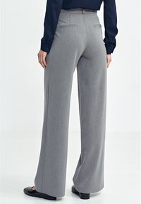 Szare spodnie o szerokich nogawkach wykonane z fakturowanej tkaniny, z dwoma tylnymi kieszeniami i dopasowanym krojem, zestawione z czarnymi płaskimi butami.