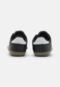 Svartvita sneakers med ovandel i läder, grå gummisula, vadderad krage och minimal sömnad på hälen. Rundad form, avslappnad design.