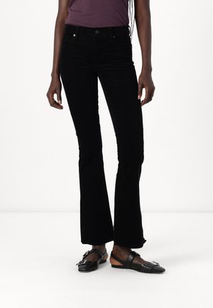 Black corduroy flared trousers with a high waistband, featuring front pockets and a smooth texture. Paired with black flat shoes.