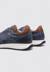 Zapatillas de cuero marino con acentos de malla, tab de talón marrón, suela de goma blanca y costuras detalladas. Vista trasera que muestra elementos de diseño.