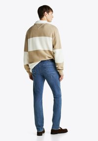 Suéter de punto a rayas en color beige y blanco con cuello, combinado con vaqueros de denim azul. Los vaqueros tienen bolsillos traseros y un corte recto.