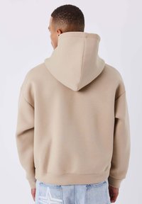 Sudadera beige con capucha, de textura suave, puños y dobladillo acanalados. Cuenta con una capucha amplia y un ajuste relajado.
