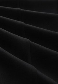 Black fabric with a smooth texture and several deep folds, showcasing a uniform color and subtle sheen. No patterns or accents visible.