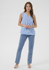 Un top sans manches bleu clair avec un motif abstrait blanc, comportant un décolleté en V et un détail de bouton, associé à un jean bleu à jambes droites.