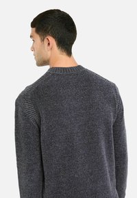 Tamno sivi pleteni pulover s okruglim izrezom, koji ima teksturiranu tkaninu, rebraste detalje na ramenima i opušteni kroj.