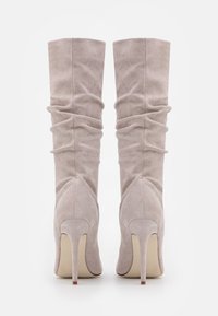 Kozaki z zamszu w kolorze taupe, sięgające do kolana, z opadającym fasonem, spiczastym czubkiem i wysokim obcasem w stylu stiletto, z marszczonym detalem wzdłuż cholewki.