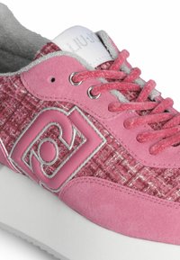 Sneaker rosa con tomaia in tessuto testurizzato e accenti in suede. Presenta un logo prominente e lacci grigi. Suola intermedia bianca con una finitura liscia.