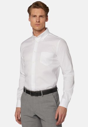 Witte button-down shirt met een enkele borstzak, getailleerde pasvorm en lange mouwen. Gecombineerd met grijze gestructureerde broeken en een zwarte riem.