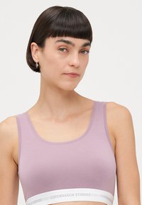 Lilac crop top in soft cotton material with a rounded neckline and wide straps, featuring a white branded elastic band at the hem.
