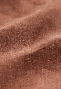 Tissu tissé marron avec une surface texturée, présentant de subtiles variations de couleur et une finition douce et mate.