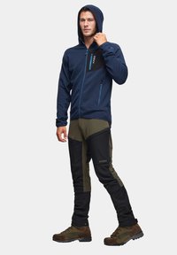 Granatowy hoodie z kapturem, z przodu na zamek błyskawiczny i kontrastową czarną kieszenią na piersi; zestawiony z oliwkowymi i czarnymi spodniami oraz brązowymi butami trekkingowymi.