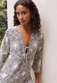 Loose-fitting, black and white patterned top with a V-neck and tie front. Features geometric designs and wide sleeves. Soft fabric texture.