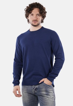 Maglione blu navy a maniche lunghe in un materiale a maglia texturizzata, con scollo rotondo e polsini a costine, abbinato a jeans chiari con effetto usurato.