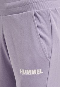 Lila Sweatpants mit einem gerippten Bund, Seitentaschen und einem weißen Logo mit "HUMMEL SPORTSWEAR SINCE 1923" nahe dem Saum. Weicher Stoff.