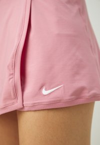 Rosa Sportrock aus glattem Material mit einem gerippten Bund, auf dem Saum mit dem weißen Nike-Swoosh-Logo.