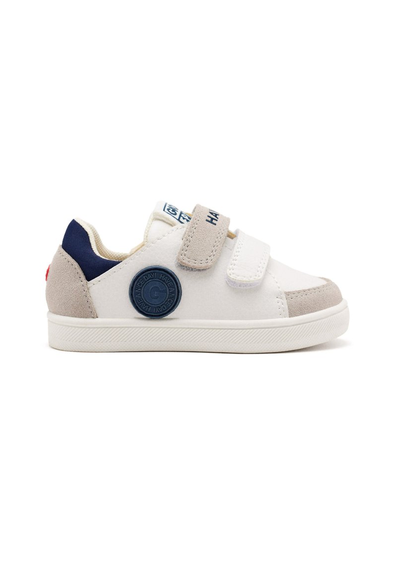 Sneaker in tessuto bianco con cinturini in velcro, dettagli in suede grigio e un logo circolare blu. Suola in gomma a profilo basso con dettagli testurizzati.