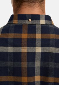 Marineblå rutete skjorte med linjer i tan, beige og grå, med en knappdetalj på baksiden av kragen og en myk, teksturert stofffinish.