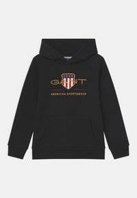 Sudadera negra con capucha y bolsillo delantero tipo canguro, con un logo bordado de un escudo con franjas rojas y blancas y texto dorado. Textura suave.