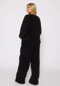 Ensemble de loungewear en polaire noire comprenant un haut à manches longues et un pantalon large avec une finition douce et texturée, offrant un look confortable.