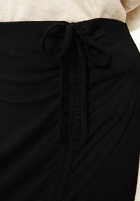 Tela negra con una cintura fruncida y detalle de cordón ajustable. Textura suave con un ligero estiramiento, diseñada para ofrecer comodidad y ajuste.