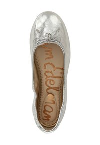 Ballerine métallique argentée avec un bout arrondi, un nœud décoratif et une texture subtile. L'intérieur comporte une semelle en tan avec le nom de la marque en écriture cursive.