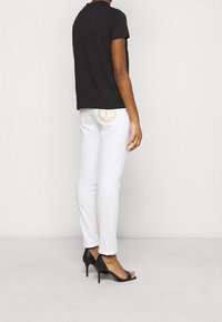 Mustat lyhythihaiset t-paidat, valkoiset slim-fit-housut, joissa on pyöreä logopatch takataskussa, yhdistettynä mustiin korkokenkiin.