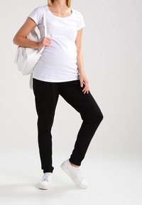 Bílá krátká tričko s krátkým rukávem, černé tepláky a bílé tenisky. Oblečení je neformální, s jednoduchým designem a volným střihem.