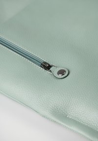 Mintgroene leren ritszak met een gestructureerd oppervlak, voorzien van een contrasterende blauwe rits en details in zilver.