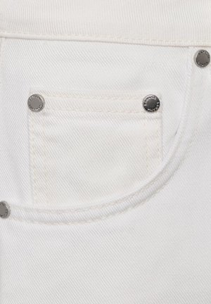 Zbliżenie na białą tkaninę dżinsową, pokazującą małą przednią kieszeń z srebrnymi nitami i szczegółowym przeszyciem.