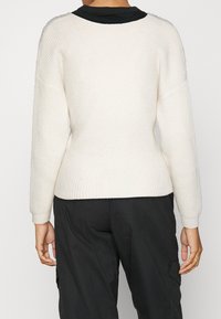 Krämmig, ribbad stickad tröja med rund halsringning, långa ärmar och en åtsittande nederkant, kombinerad med mörka cargobyxor.