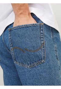 Jeans i denim med en bakficka med dekorativ sömnad, ett blått strukturerat tyg och synliga hårdvarudetaljer.