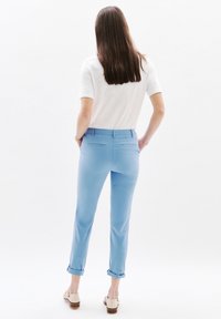 Helle blaue Chinos mit hochgekrempelten Säumen, hinteren Taschen und slim fit, kombiniert mit einem kurzärmligen weißen Oberteil. Glatte Stoffstruktur.