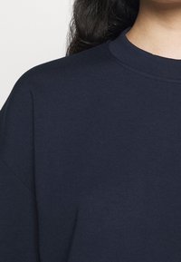 T-shirt oversize in cotone blu navy con colletto rotondo e maniche corte. Il tessuto ha una consistenza liscia e dettagli di cucitura minimi.