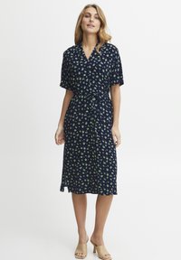 Marinblå klänning med korta ärmar, grön blommig tryck, v-ringning, midjeband och en medellång silhuett; slätt tyg, sidokslag.