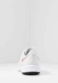 Sneaker Nike bianco con tomaia testurizzata, logo swoosh rosa e suola in gomma nera. Presenta un'etichetta a loop per una facile calzata.