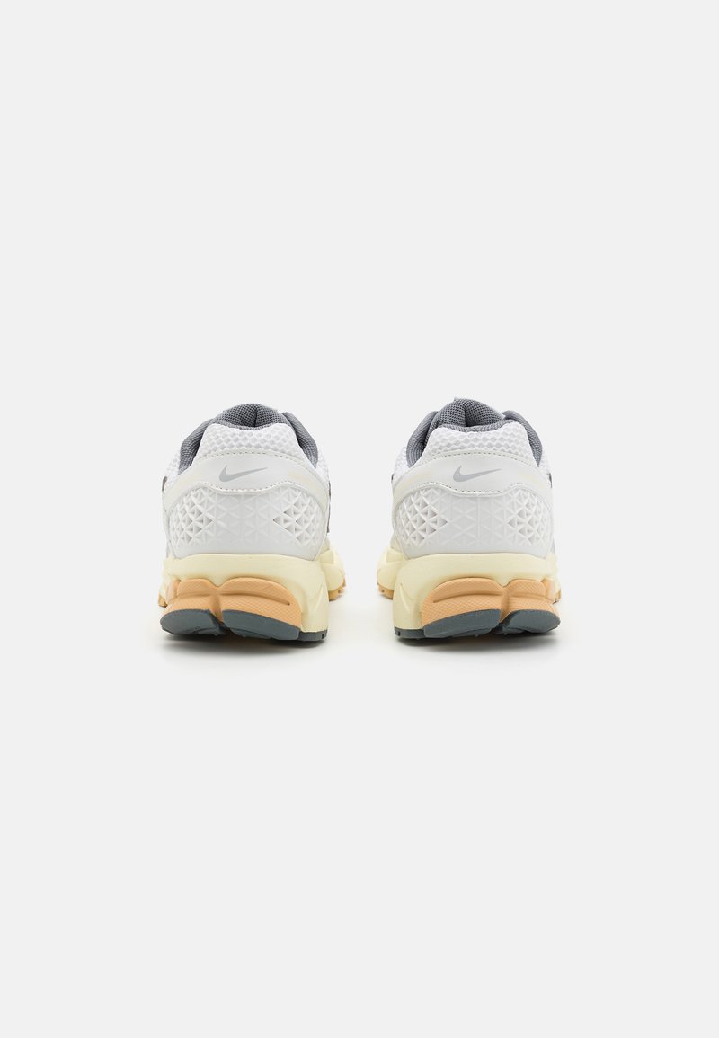 Nike sneakers met een witte mesh bovenkant, grijze accenten, een gevoerde zool in oranje en beige, en een geometrisch patroon op de hak.