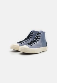 Baskets montantes en toile bleu clair avec des accents bleu foncé, lacets noirs et coque et semelle en caoutchouc blanc. Détail de couture texturée.