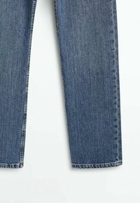Rakt skurna blå denimjeans ben visade från mitten av låret till fållen på en vit bakgrund.
