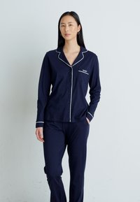 Conjunto de pijama de algodão azul-marinho com uma camisa de botões com contornos brancos e um bolso no peito, acompanhada por calças combinando.
