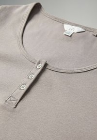 Hellgraues Baumwoll-T-Shirt mit Rundhalsausschnitt, drei Druckknöpfen und kurzen Ärmeln. Glatte Textur mit subtilen Nahtdetails.
